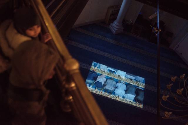 Female congregation members look down on moving projection in main prayer hall at Brick Lane Mosque